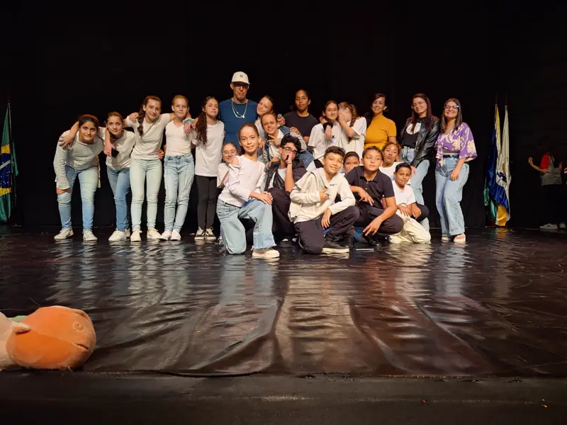 Grupo de adolescentes e educadores no palco de um teatro, depois de uma apresentação