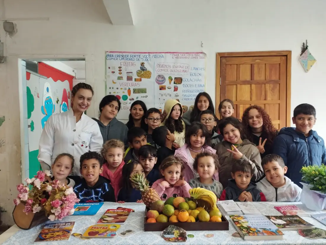 Crianças e educadoras da ACRICA reunidas em volta de uma mesa com frutas