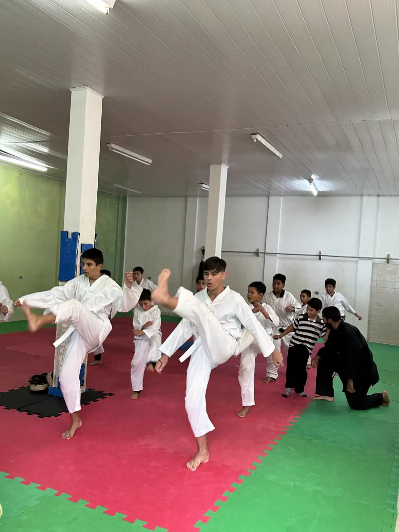 Alunos de quimono treinando chutes numa aula de taekwondo